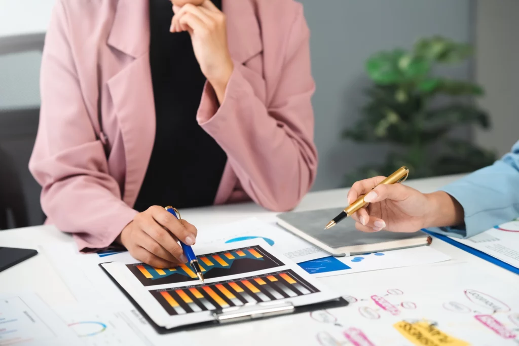 Two professionals in business attire pointing at bar charts with pens during a financial meeting, representing CFO-driven business performance analysis.
